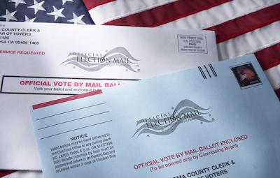 Two vote-by-mail envelopes lying on a US flag backdrop