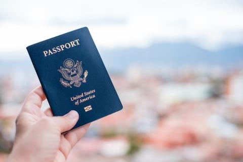 hand holding US passport in front of view of blurred red-roofed buildings